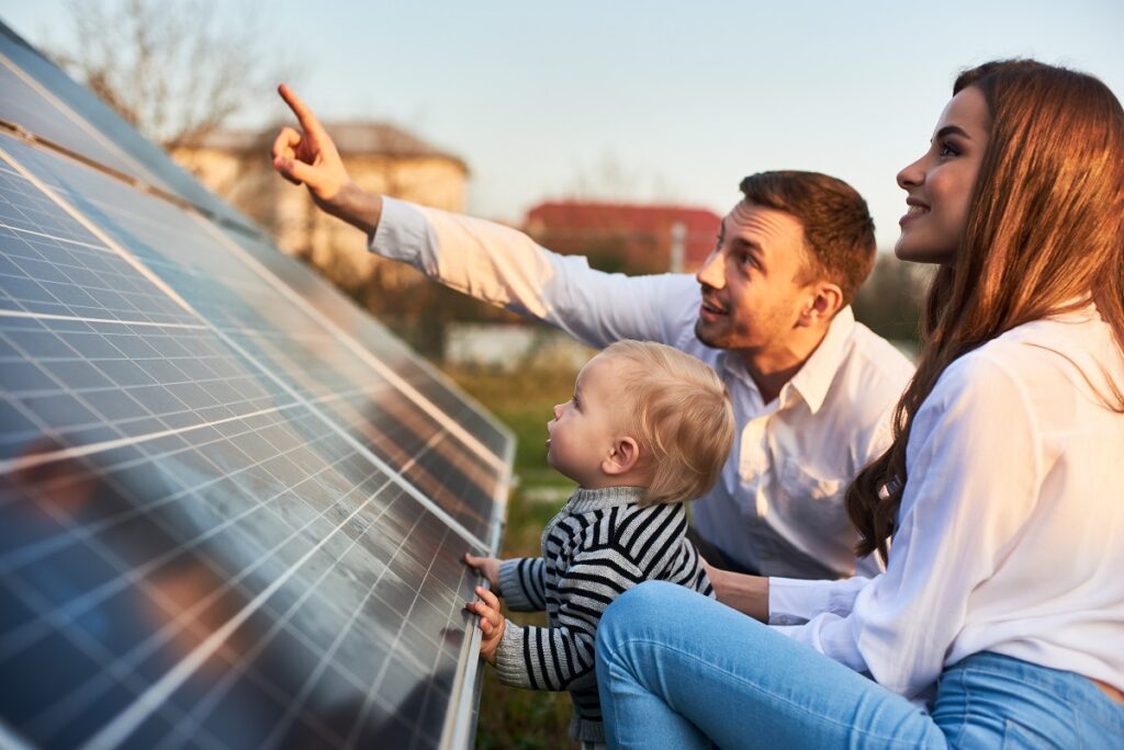 a mother, father, and toddler looking at a solar panel on the ground