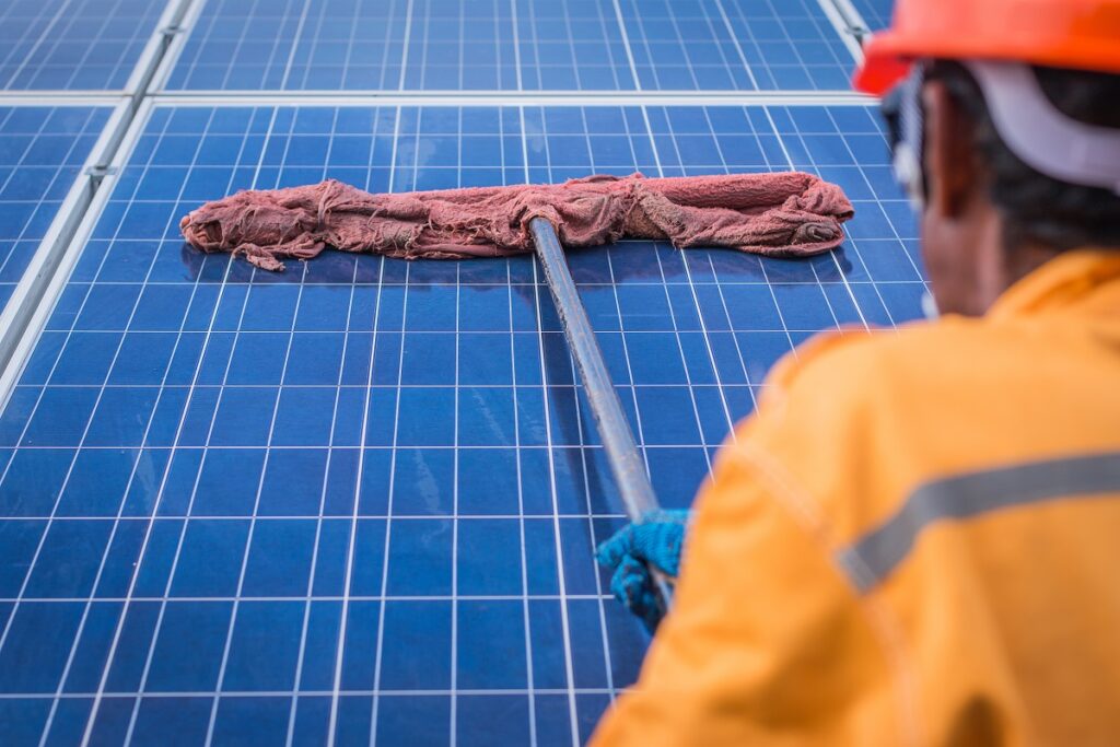 a maintenance worker wiping a solar panel with a mop