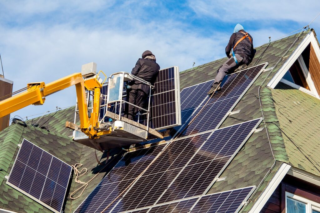 installers using a cherry picker to lift solar panels to a roof